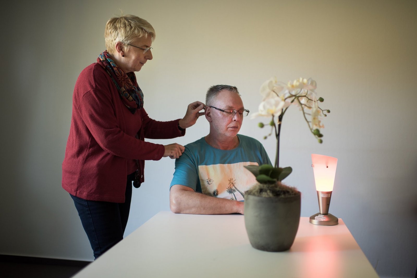 Therapeutin setzt Akupunkturnadel an das Ohr eines männlichen Patienten
