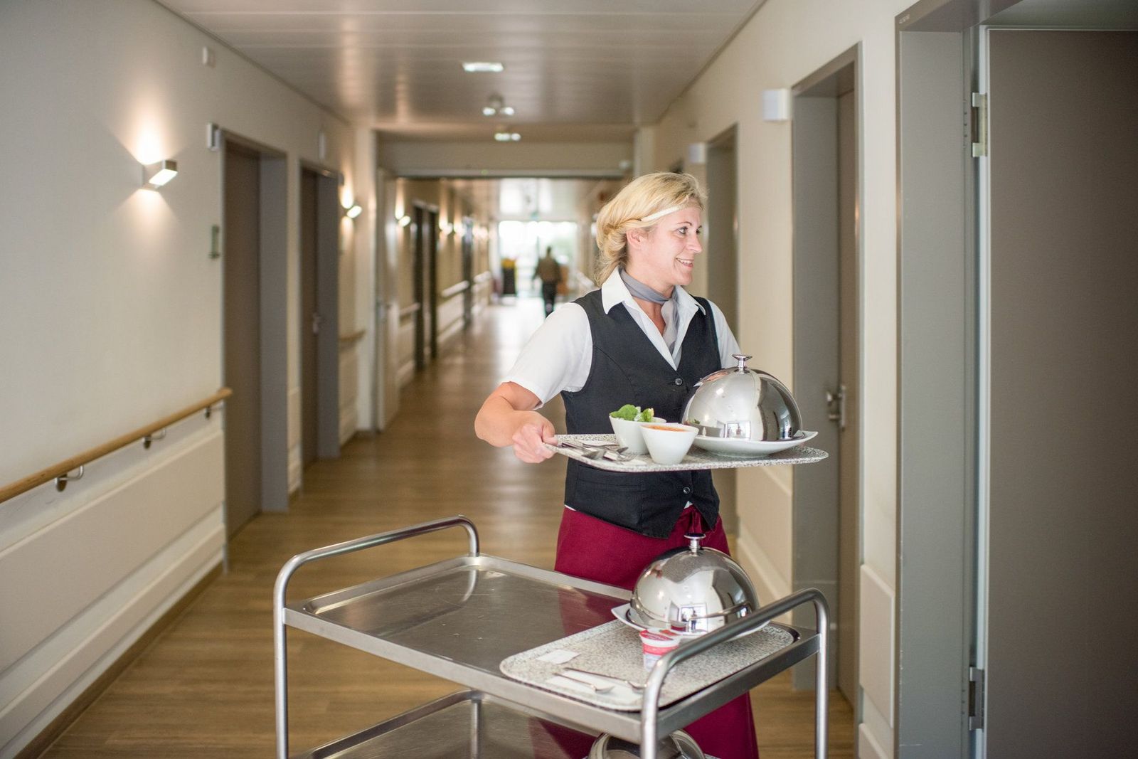 Adrett gekleidete Servicemitarbeiterin bringt das Essen auf einem Tablett ins Patientenzimmer