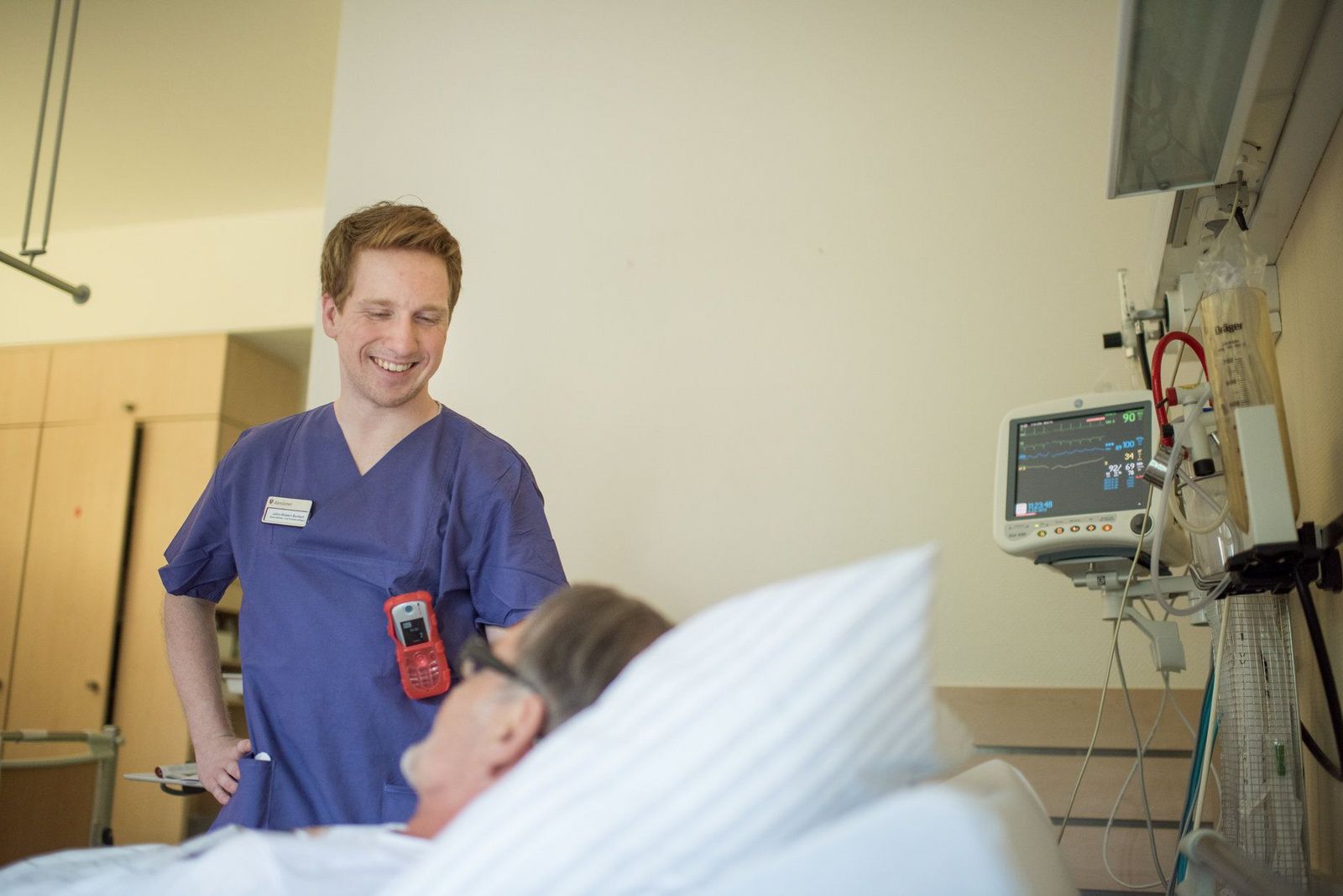 Freundlich lächelnder Krankenpfleger im Gespräch mit einem Patienten am Krankenbett