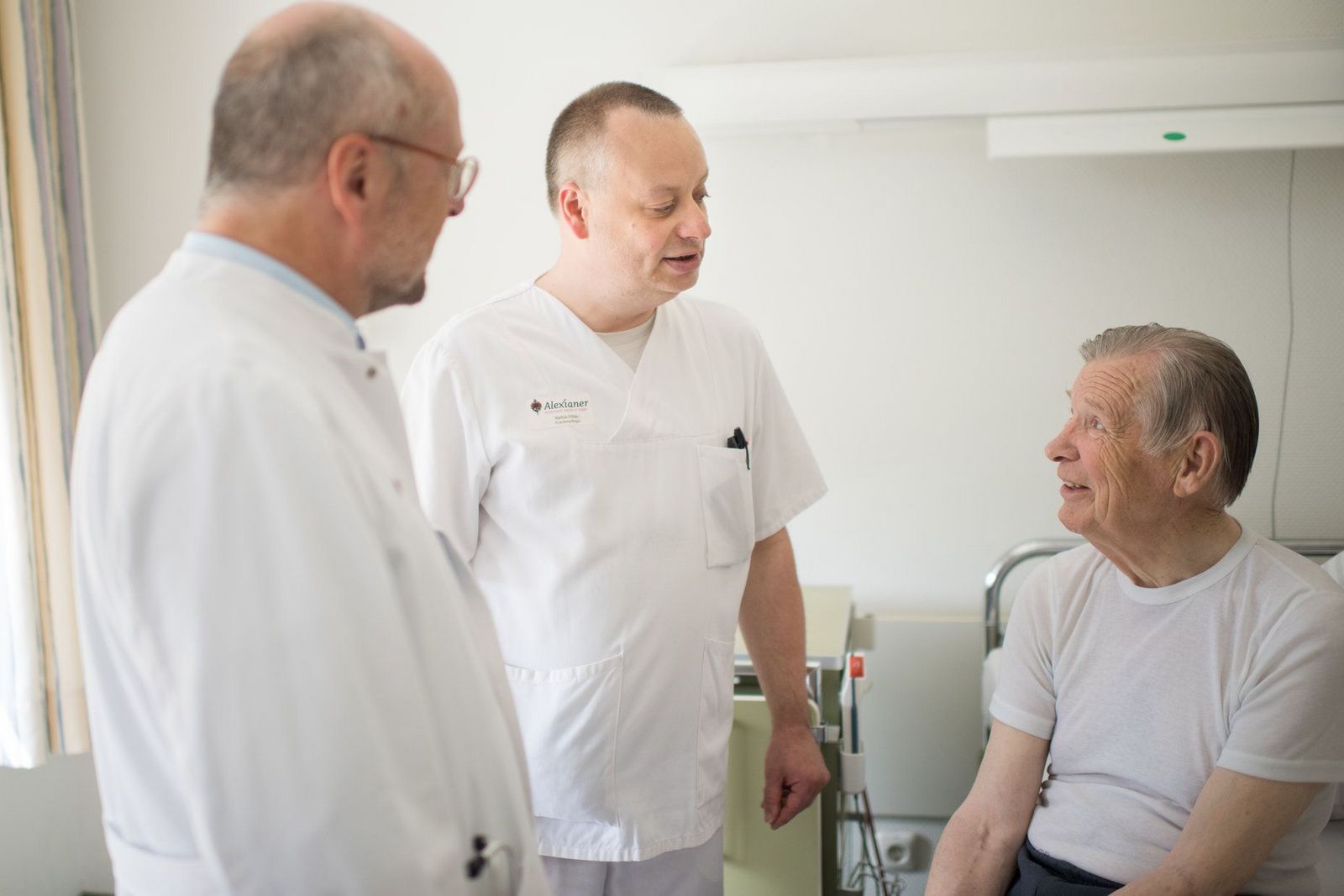 Arzt und Krankenpfleger im Gespräch mit älteren Patienten am Patientenbett während der Visite