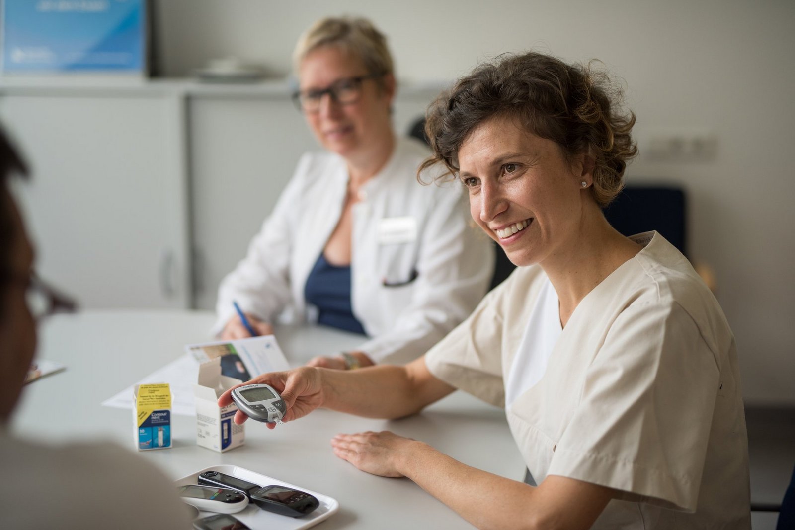 Pflegekraft und Ärztin erklären der Patientin das Blutzuckermessgerät