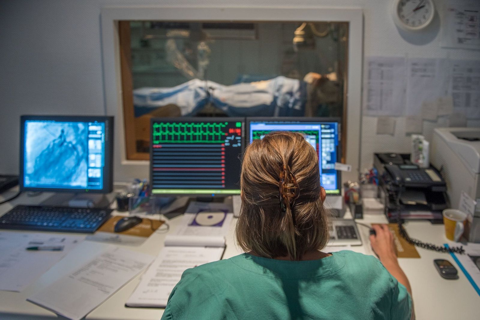 Untersuchung im Linksherzkatheterlabor: Eine Pflegekraft betrachtet während der minimal-invasiven Untersuchung das Ergebnis auf dem Bildschirm