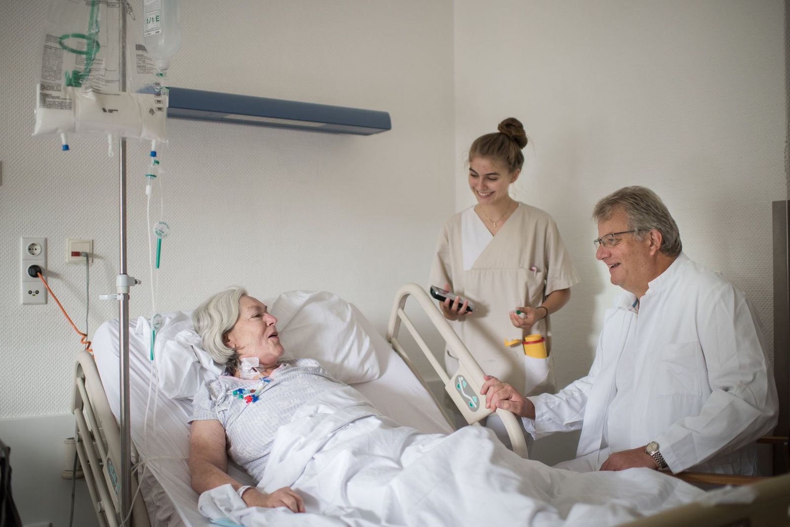 Arzt und Krankenschwester im Gespräch mit einer im Bett liegenden Patientin