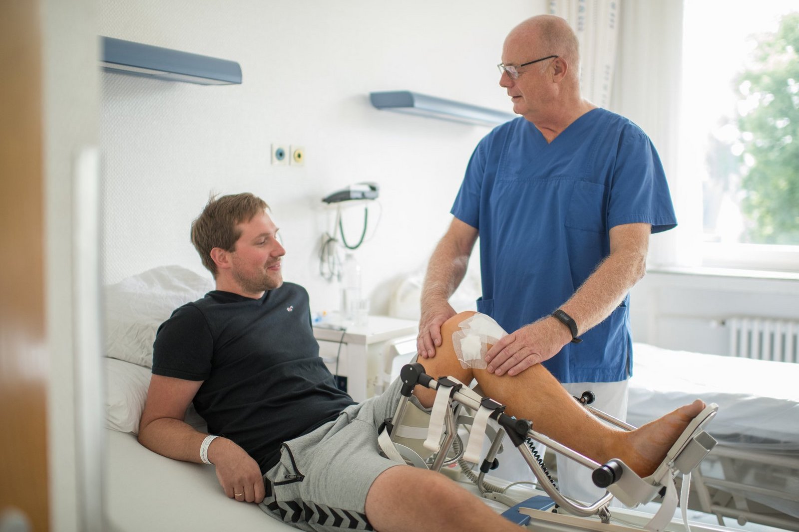 Nachuntersuchung nach Knie-OP durch Arzt am Patientenbett. Arzt tastet Knie ab. Nachuntersuchung nach Knie-OP durch Arzt am Patientenbett. Arzt tastet Knie ab.